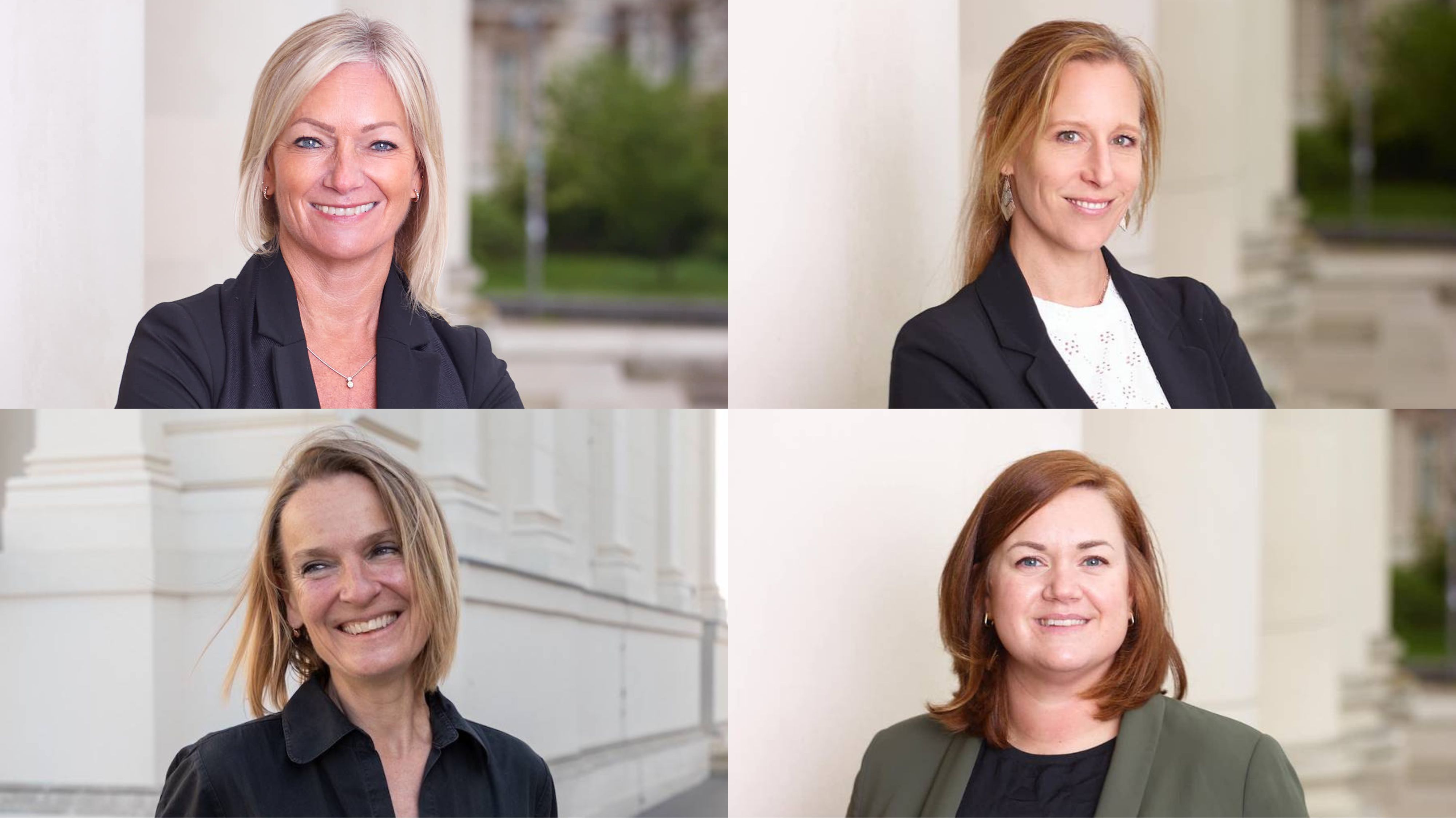 Four women in business attire are smiling at the camera in front of a building with columns.