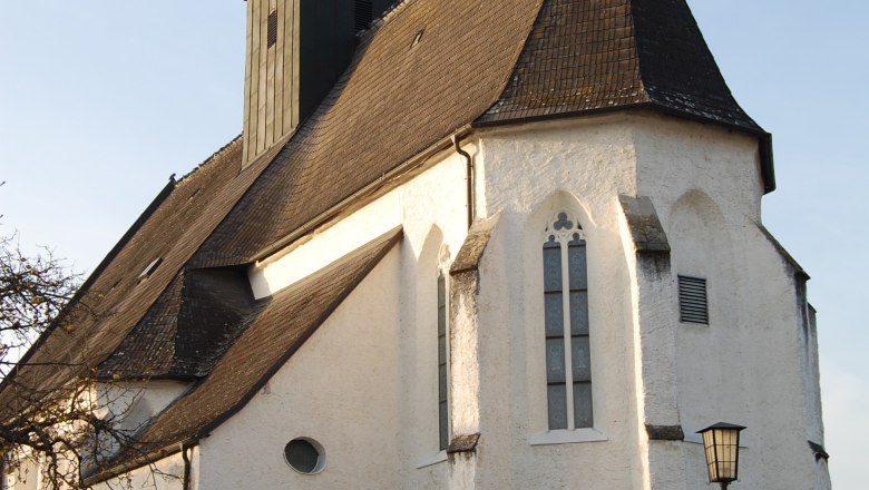 Totzenbach parish church with clock tower and pointed roof, surrounded by a fence, in daylight.