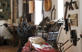 Innenansicht eines Heimatmuseums mit alten Werkzeugen und einem roten Kinderwagen.