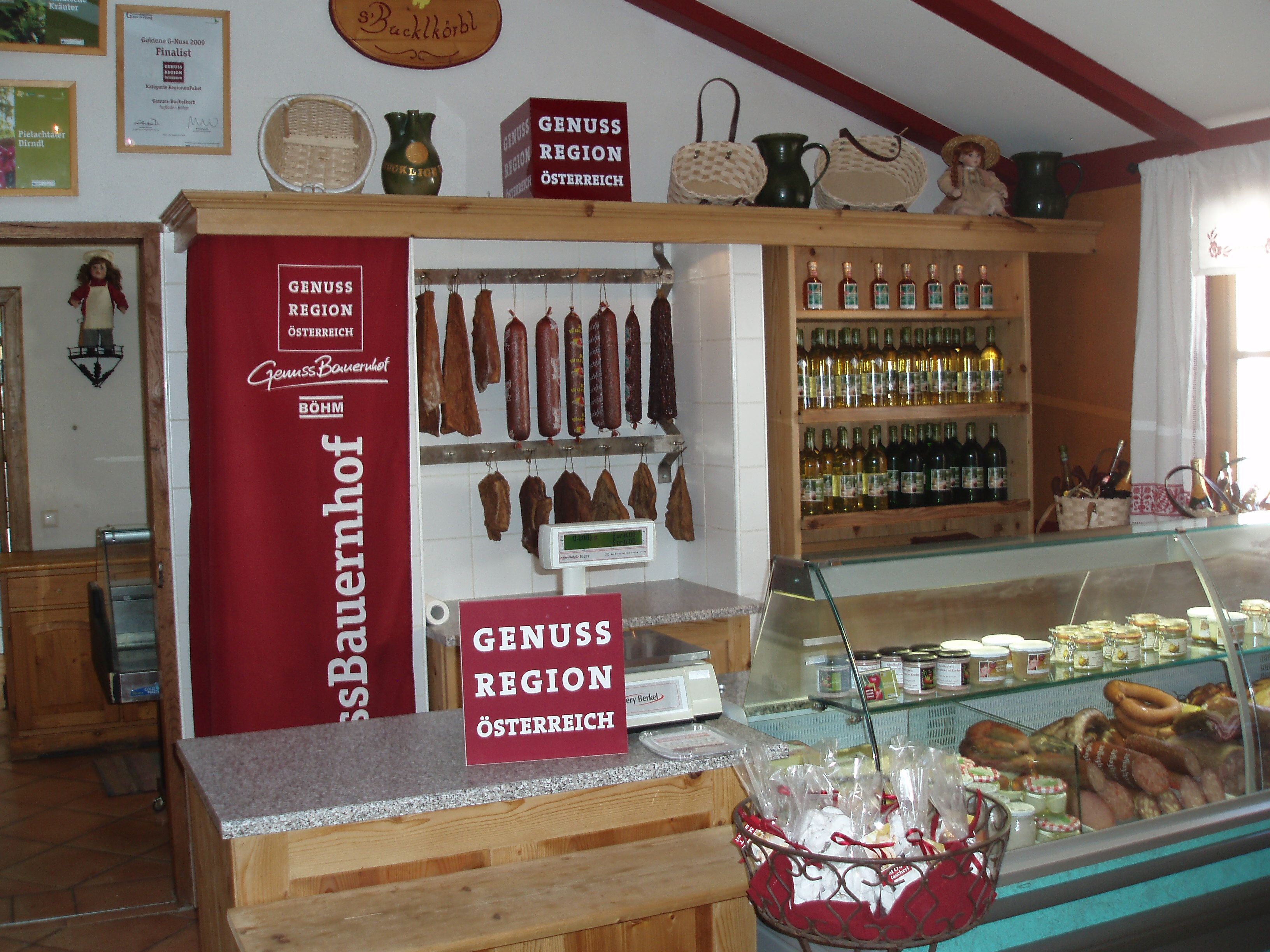 Innenansicht eines Hofladens mit Wurstwaren, Weinflaschen und einem Kühlregal.