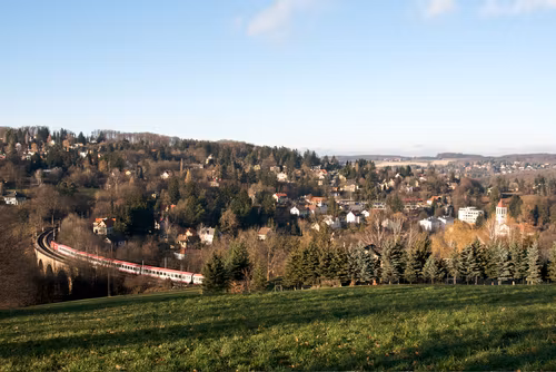 Landschaft mit Zug auf Viadukt in Eichgraben, umgeben von Hügeln und Häusern.