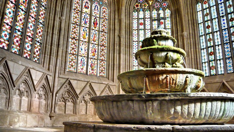 Ein alter Brunnen in einem gotischen Gebäude mit bunten Glasfenstern.