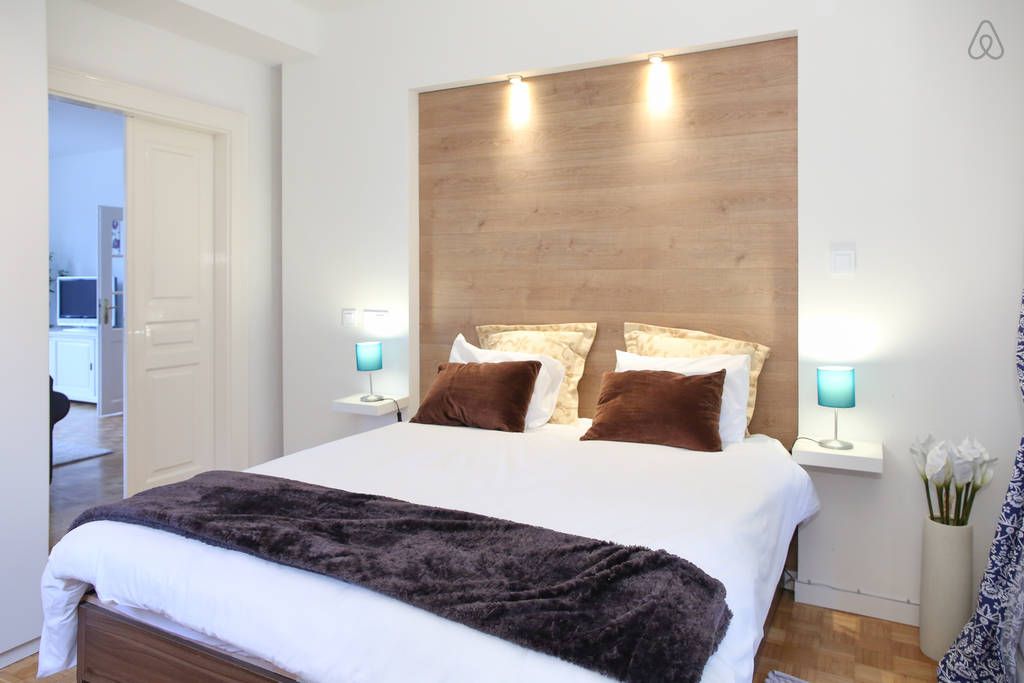 Modernes Schlafzimmer mit Doppelbett, Holzrückwand und blauen Nachttischlampen.