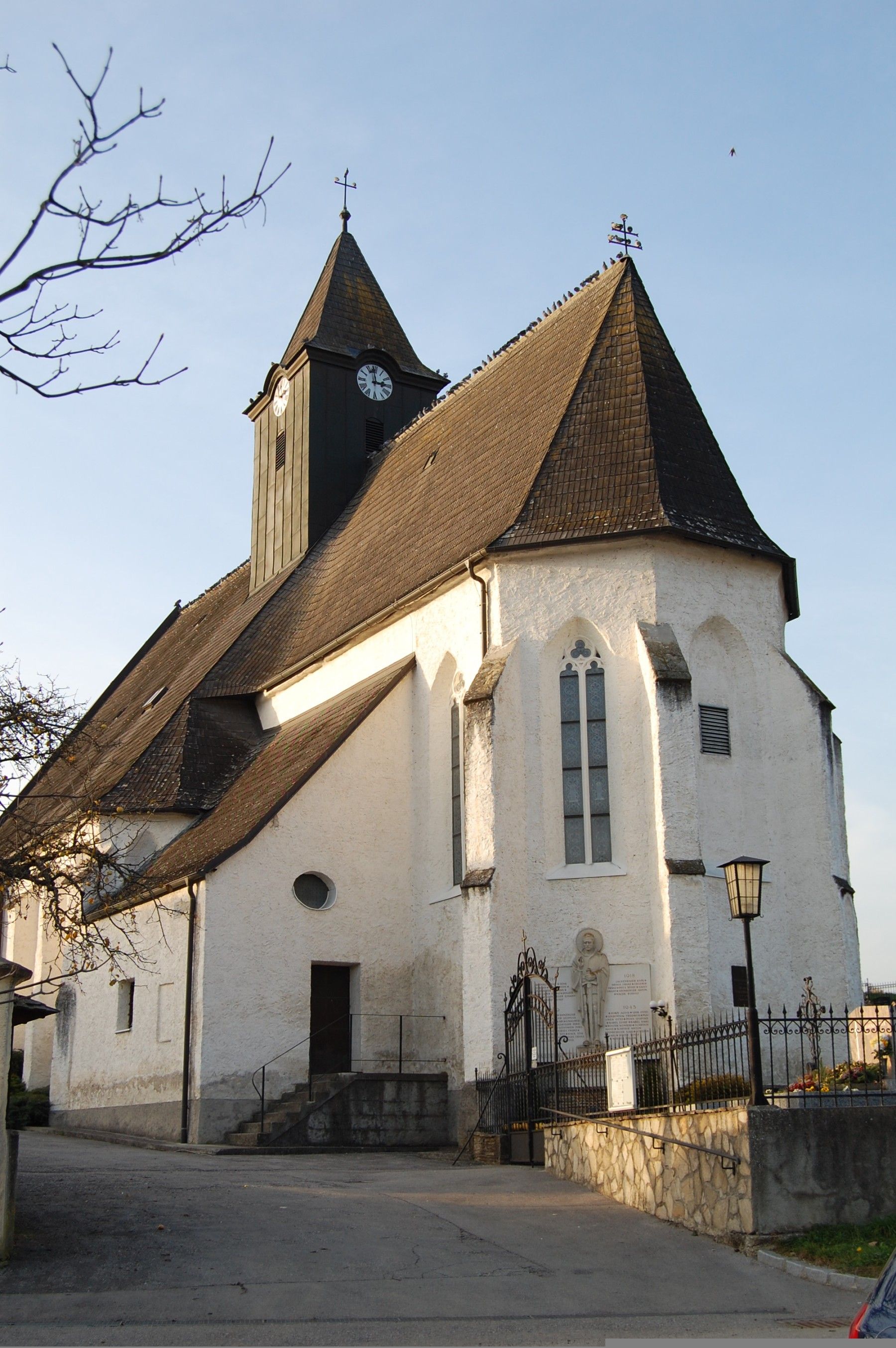 Pfarrkirche Totzenbach mit Uhrturm und Spitzdach, umgeben von einem Zaun, bei Tageslicht.