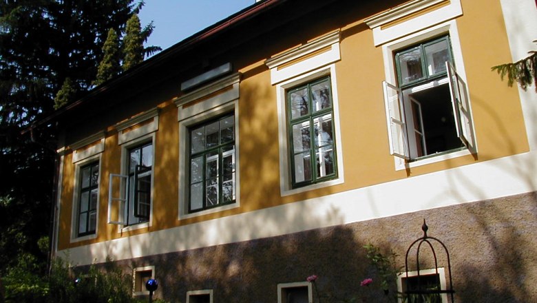 Gelbes Haus mit offenen Fenstern und Garten im Vordergrund.