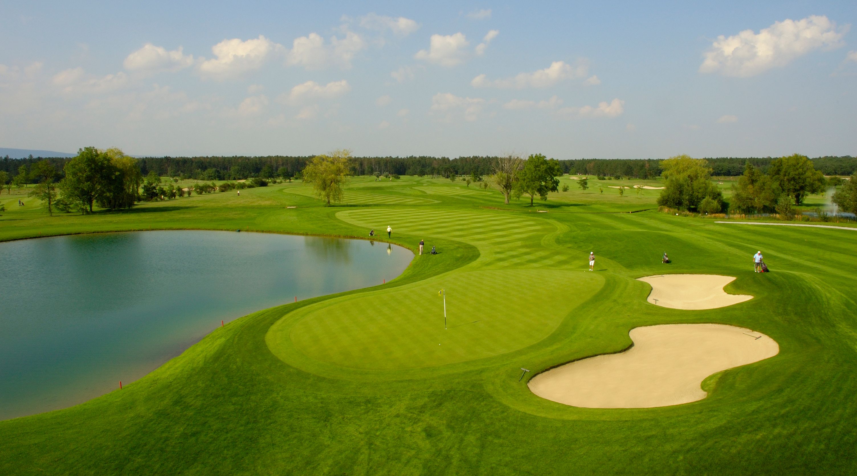 Golfplatz mit Teich, Sandbunker und Spielern.