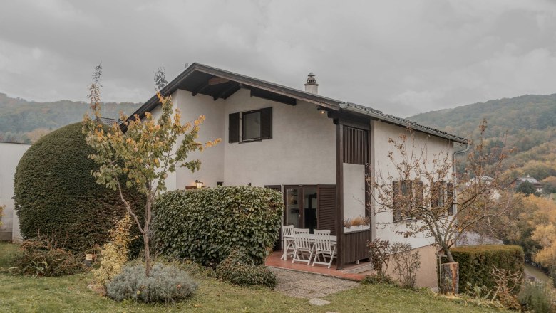 Ein zweistöckiges Haus mit Garten und Terrasse, umgeben von Bäumen und Sträuchern.