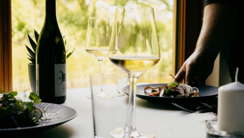 A laid table with a bottle of wine, wine glasses and a plate of food in a restaurant.