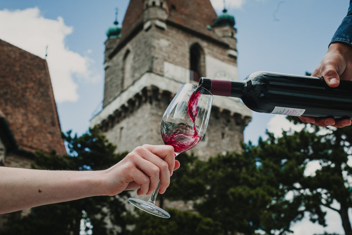 Während Rotwein sanft ins Glas fließt, zeigt sich im Hintergrund die Burg Perchtoldsdorf in eindrucksvoller Nähe.