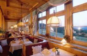 Gemütliches Restaurant mit Holzeinrichtung und großen Fenstern mit Blick auf die Landschaft.