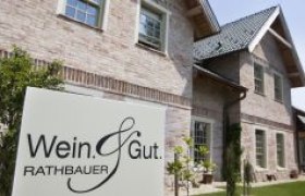 Ein Schild mit der Aufschrift 'Wein & Gut Rathbauer' vor einem Backsteingebäude.