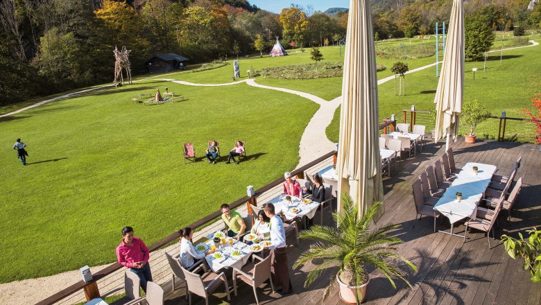 Terrasse des Seminar- und Eventhotels Krainerhütte mit Gästen beim Essen, umgeben von grüner Wiese und Wald.