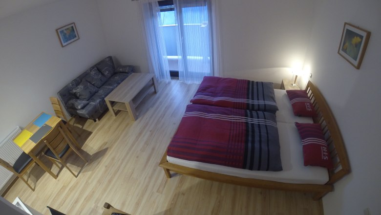 A simply furnished apartment with a bed, sofa, table and chairs.