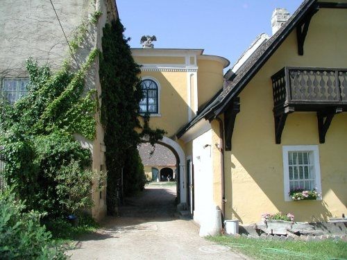 Ein gelbes Gebäude mit einem Torbogen, umgeben von Efeu und einem kleinen Balkon.