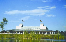 Gebäude des Golf Club Schloss Ebreichsdorf hinter einem Teich mit Schilf, blauer Himmel.