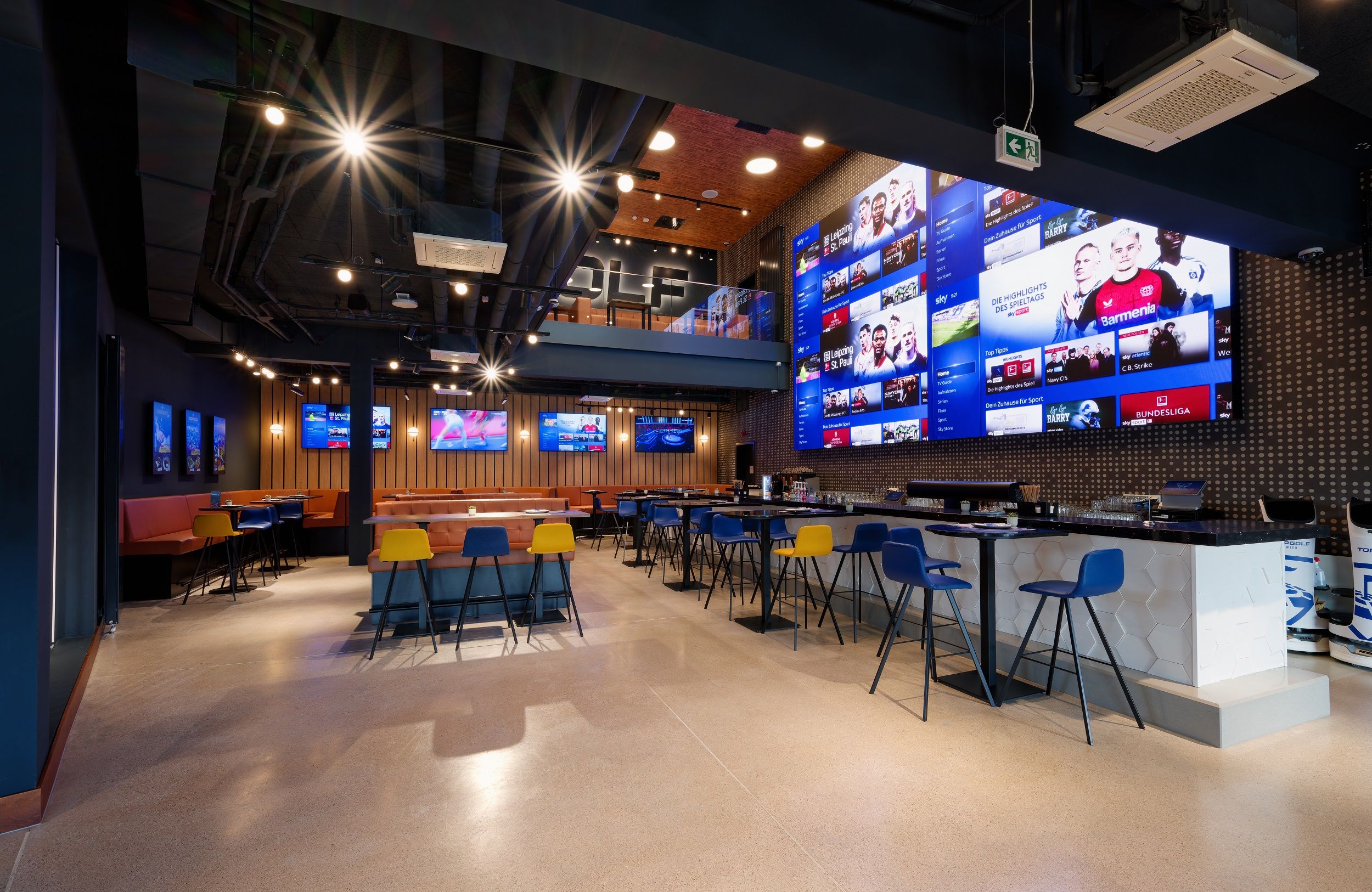 Innenansicht eines modernen Sportbars mit großen Bildschirmen und bunten Stühlen.