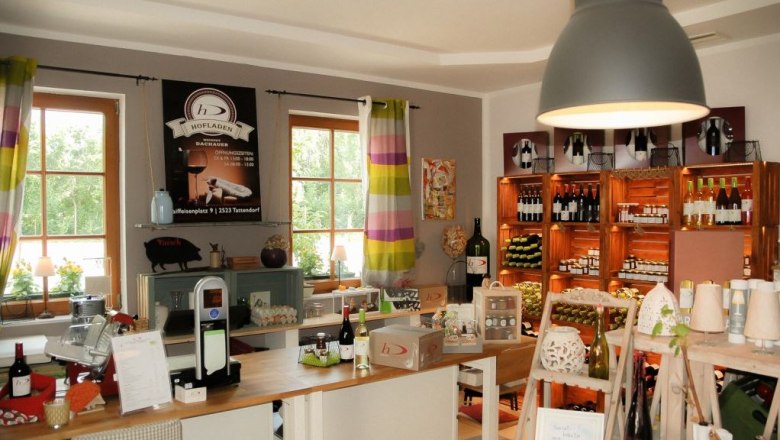 Innenansicht eines Hofladens mit Regalen voller Weinflaschen und Produkten.