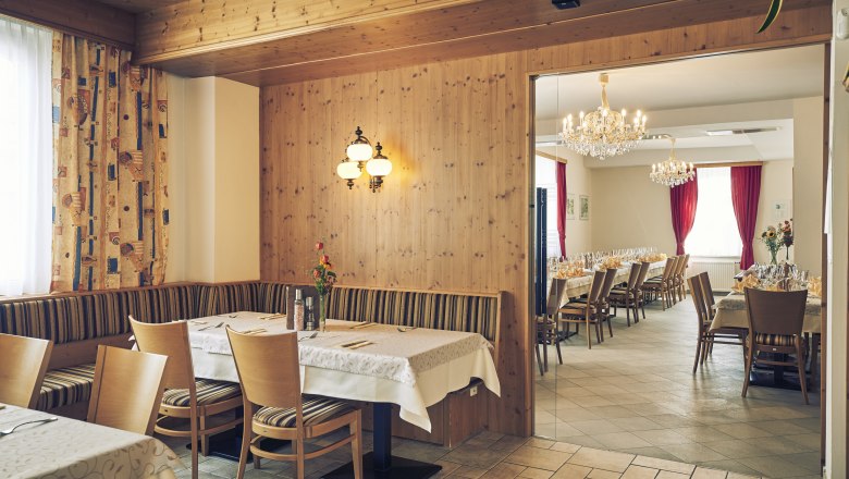 Ein gemütliches Gastzimmer mit Holzwänden und ein angrenzender Festsaal mit Kronleuchtern und gedeckten Tischen.