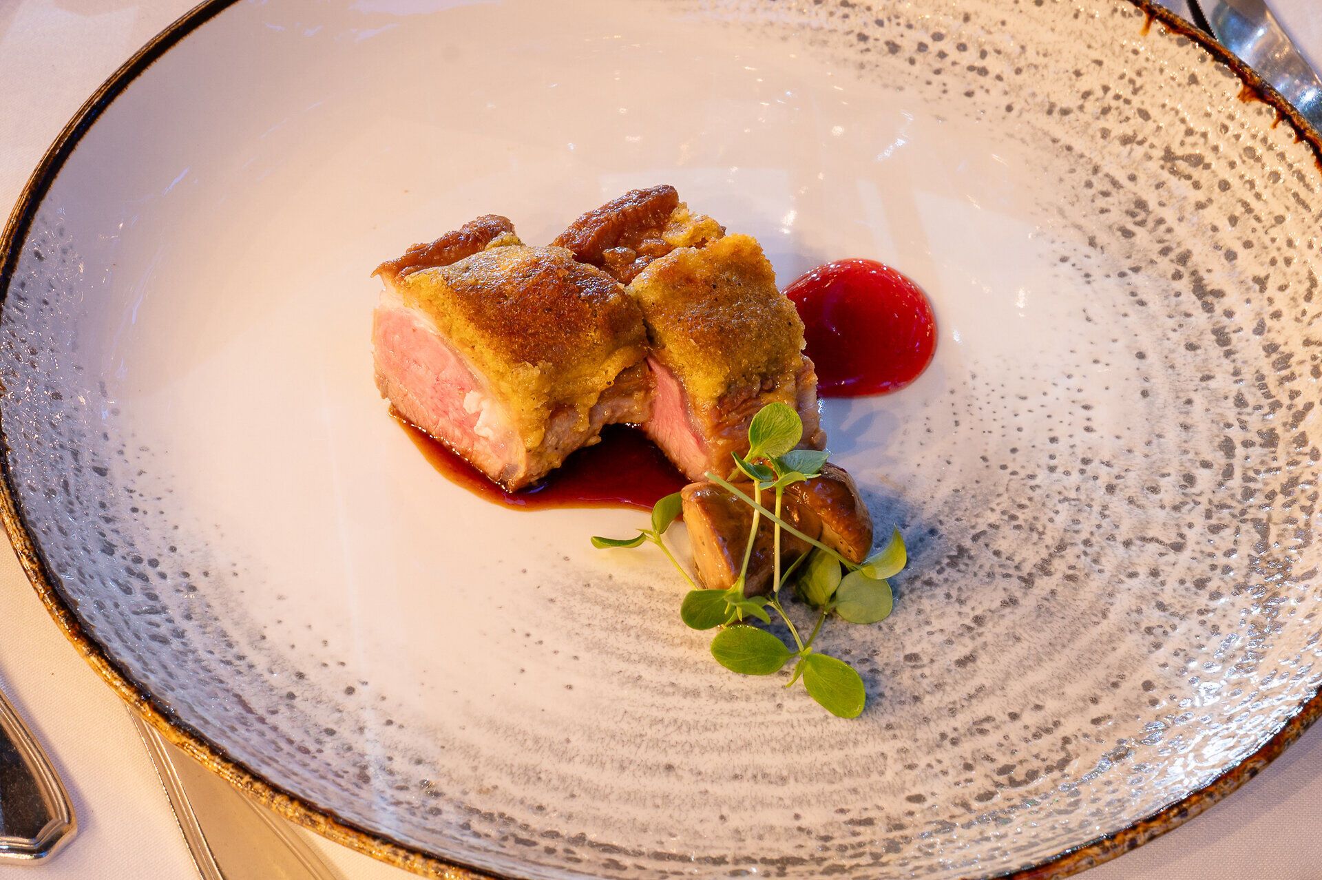 Zartes Lammfilet, kunstvoll auf einem strahlend hellen Teller arrangiert, verführt das Auge mit einer rosaroten Sauce, die wie ein flüssiger Edelstein in der Mitte thront. Geometrisch perfekt platziert, entfaltet sich ein visuelles Gedicht aus sanften Farben und klaren Linien. Das Bild fängt den Moment ein, in dem Genuss und Kunst eine geschmackvolle Allianz eingehen – eine Einladung, den Gaumen auf eine unerwartete Reise zu schicken.