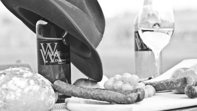 Black and white picture of wine bottles, bread, sausage and grapes on a table.