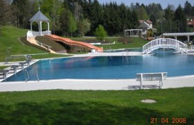 Freibad mit Rutsche, Brücke und Pavillon im Hintergrund.