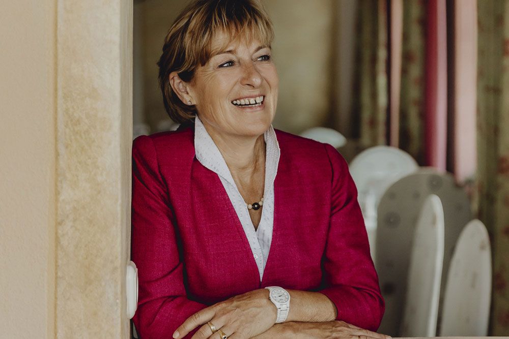 Frau in rotem Blazer lächelt und lehnt sich an eine Wand.