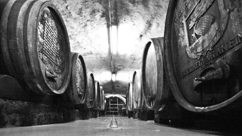 Black and white photo of a wine cellar with large wooden barrels.