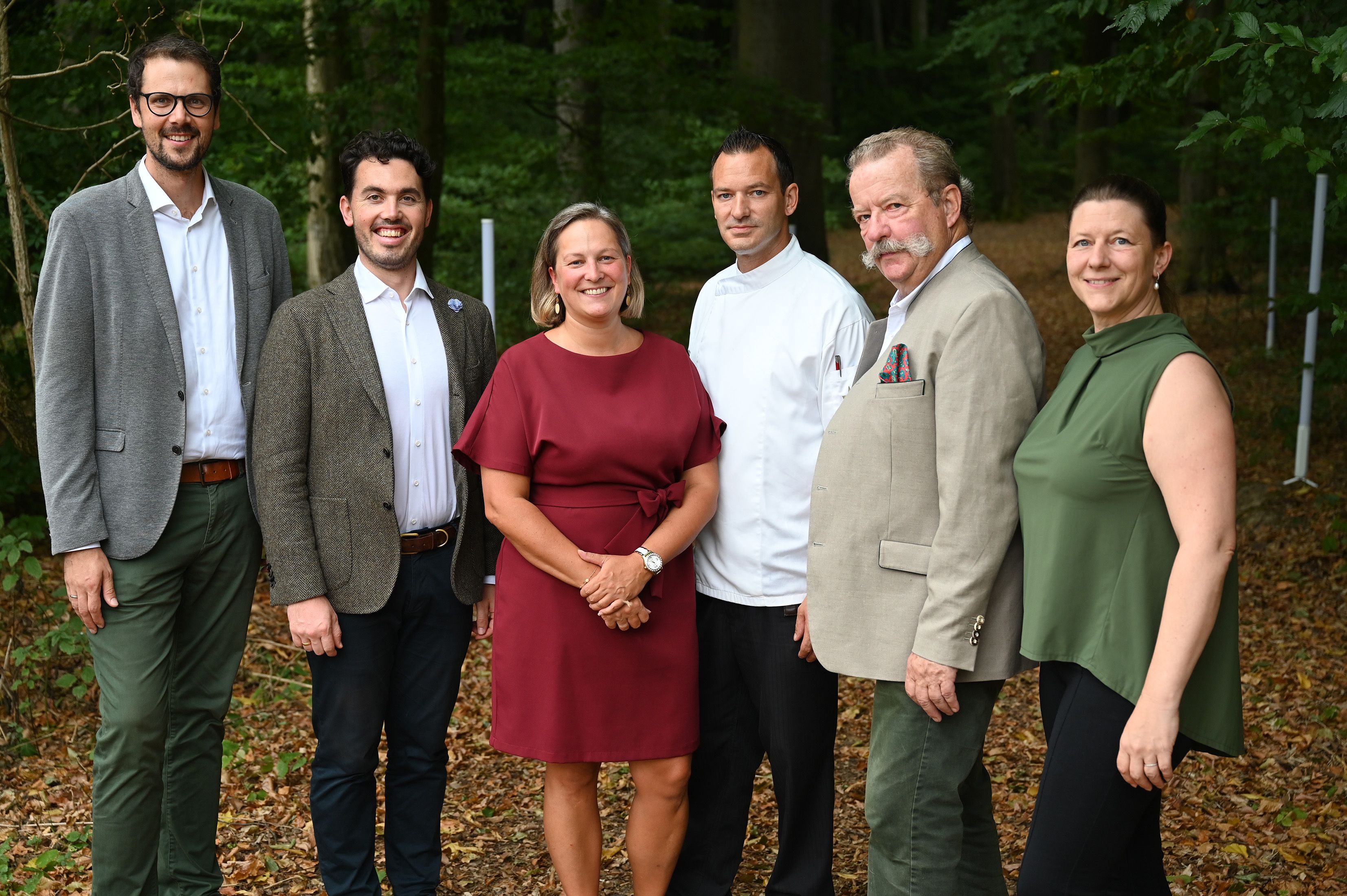 Gruppe von Personen steht vor einem Wald für ein Gruppenfoto