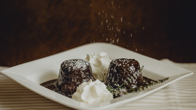 Zwei Schokoladenküchlein mit Puderzucker und Sahne auf einem Teller.