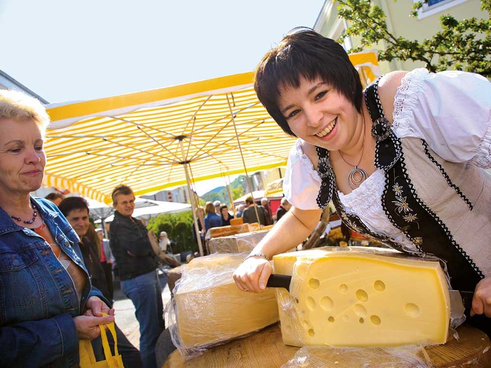Frau in traditioneller Kleidung schneidet Käse auf einem Markt.