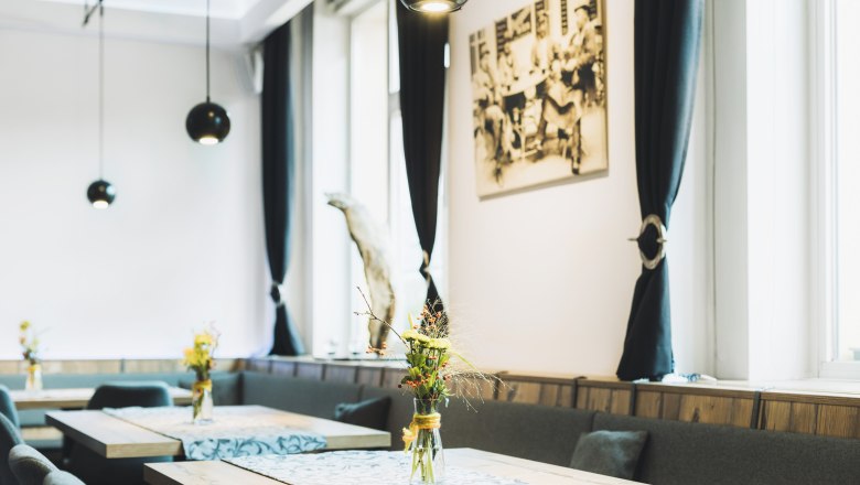 Innenansicht eines stilvollen Cafés mit Holztischen, Blumenvasen und schwarzen Vorhängen.