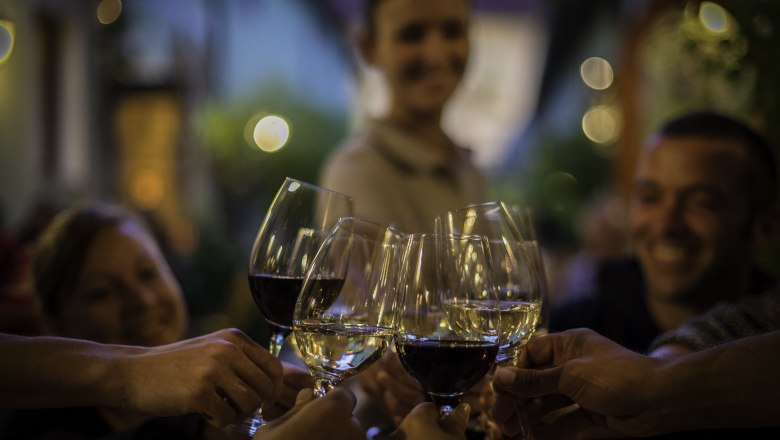 People clink glasses of wine, blurred background with lights.
