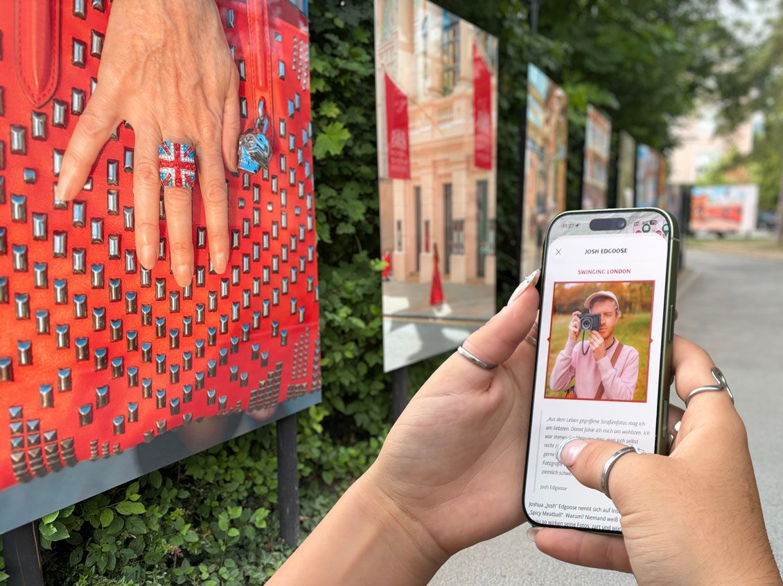 Die neue Foto-App zur Fotoausstellung La Gacilly Baden Photo wird in der Hand liegend präsentiert. Dahinter sind Fotos der Fotoausstellung La Gacilly Baden Photo zu sehen.
