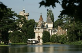 Schloss Laxenburg mit Türmen und Bäumen am Seeufer.