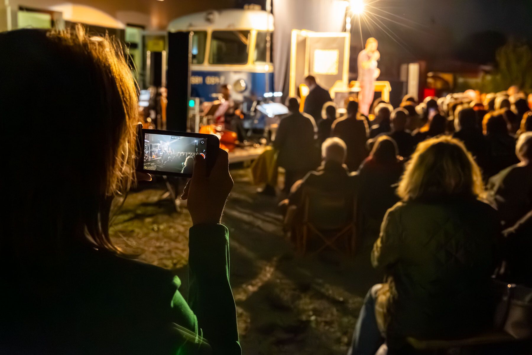 Unter dem Sternenhimmel versammeln sich Menschen, um die Klänge eines Live-Auftritts zu genießen. Die warme Atmosphäre des Kulturbahnhofs lädt dazu ein, den Abend in geselliger Runde zu verbringen und die kulturellen Highlights des Sommers zu erleben.