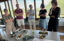 Gruppe steht vor einem Tisch auf dem Speisen kreativ zubereitet und dekoriert dargestellt werden.