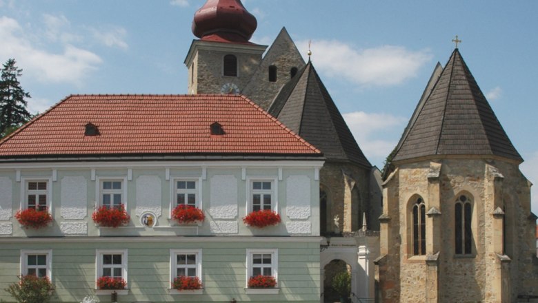 Historisches Gebäude mit rotem Dach und Kirche im Hintergrund auf dem Marktplatz Maria-Anzbach.