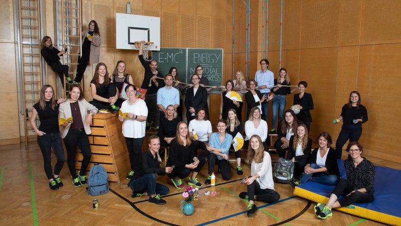 Group of people in a gym with sports equipment and blackboard in the background.