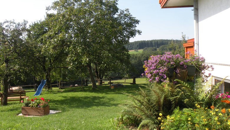 Ein grüner Garten mit Bäumen, Blumen und einer blauen Rutsche.