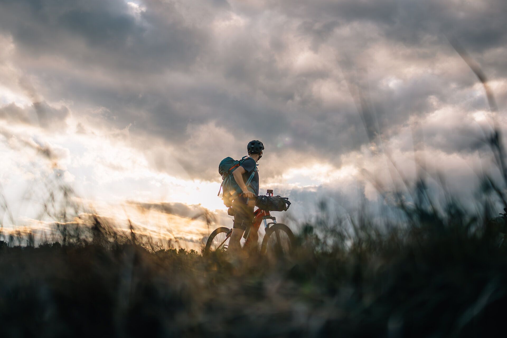 Ein Radfahrer genießt die frische Luft und die atemberaubende Aussicht auf die sanften Hügel des Wienerwaldes. Die Wolken am Himmel verleihen der Szenerie eine dramatische Note, während die Natur in voller Blüte steht. Diese friedliche Umgebung lädt dazu ein, die Seele baumeln zu lassen und die Schönheit der Landschaft zu erkunden.