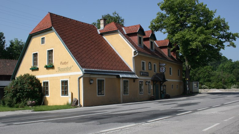 Gelbes Gasthaus mit rotem Dach an einer Straße, umgeben von Bäumen.
