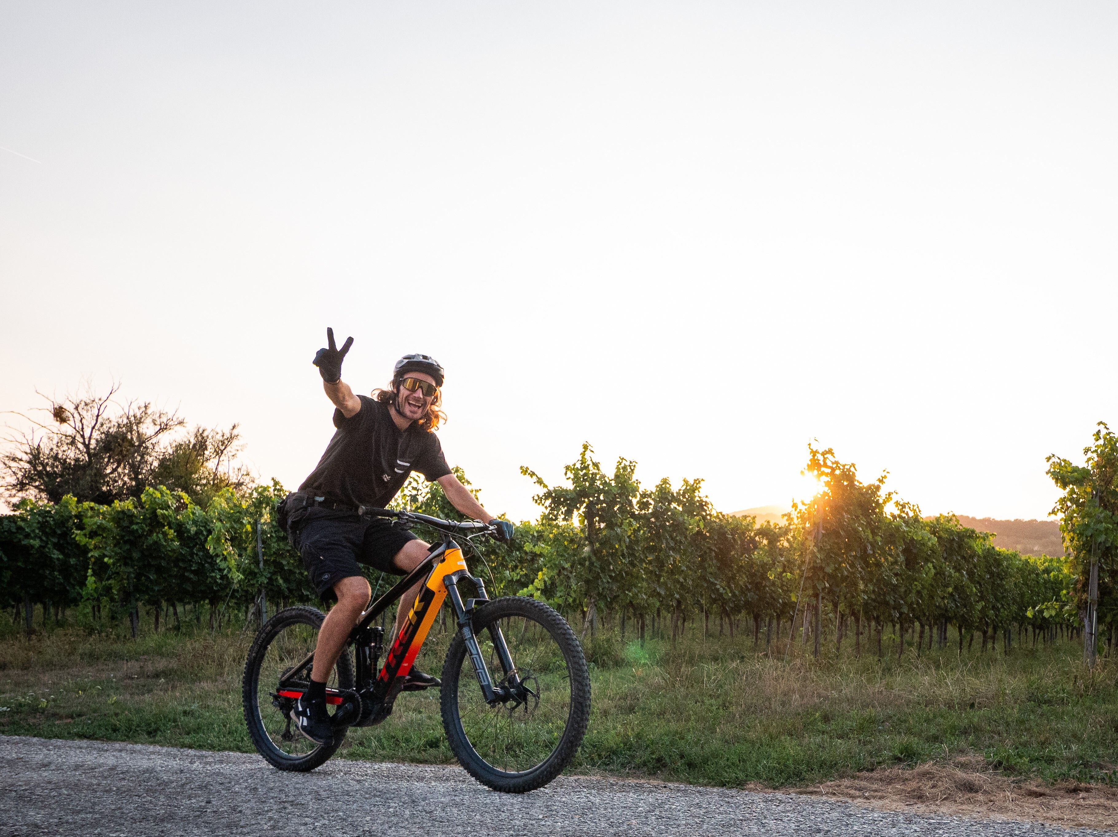 Ein fröhlicher Mountainbiker genießt die sanften Hügel des Wienerwaldes, während die Sonne langsam am Horizont untergeht. Die malerische Landschaft mit Weinreben und sanften Wiesen schafft eine perfekte Kulisse für Abenteuer und Entspannung. Hier wird der Sommer in den Bergen zum unvergesslichen Erlebnis.
