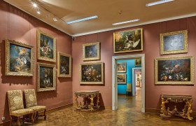 A room in the museum with paintings on the walls and antique furniture.