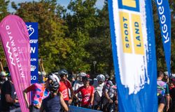 Gruppe von Radfahrerinnen und Radfahrern mit Gravelbikes zwischen bunten Veranstaltungsbannern unter freiem Himmel.