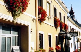 Ein traditionelles Gasthaus mit gelber Fassade und roten Blumen an den Fenstern.