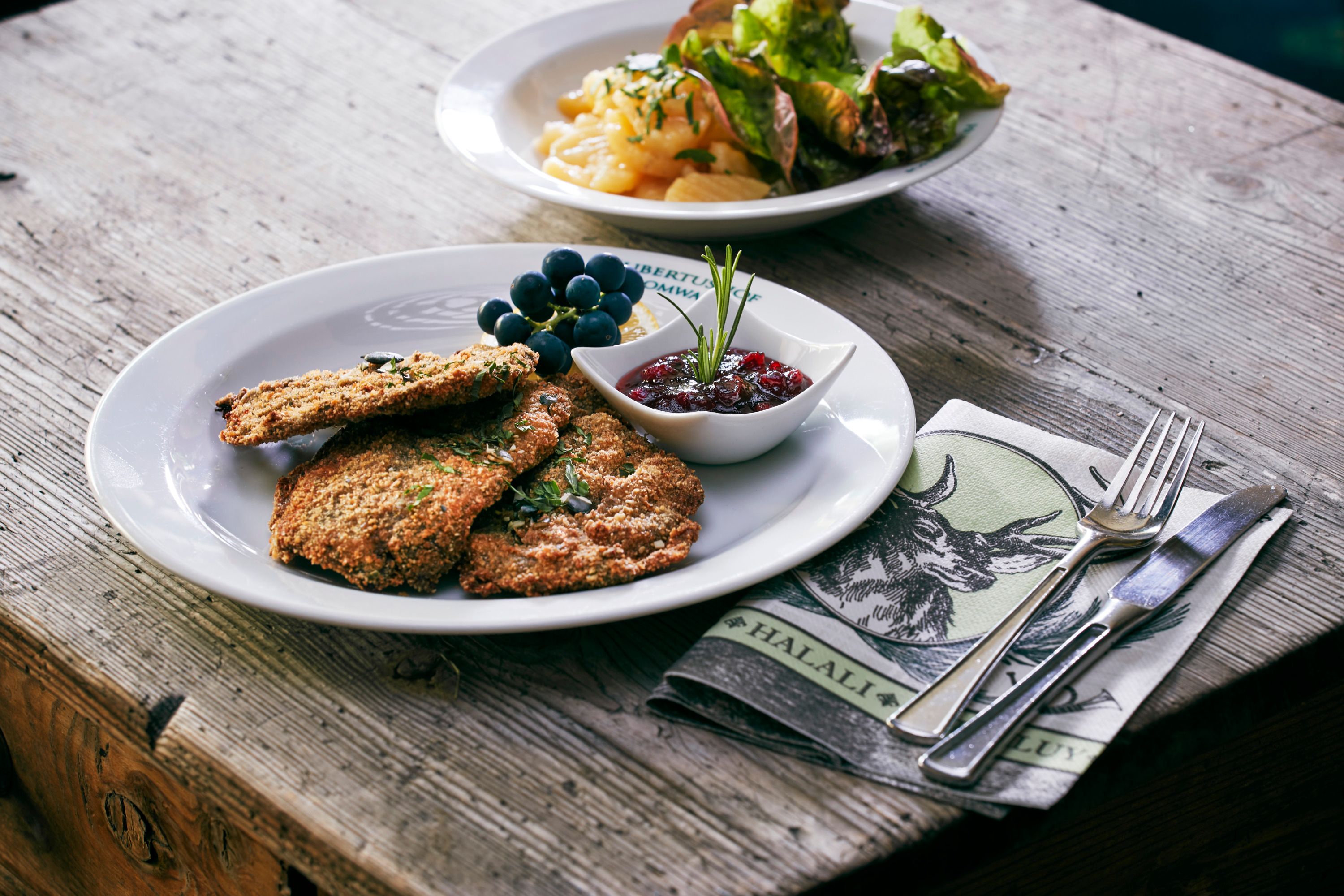 Ein Teller mit Rehschnitzel, Preiselbeeren und Trauben auf einem Holztisch.