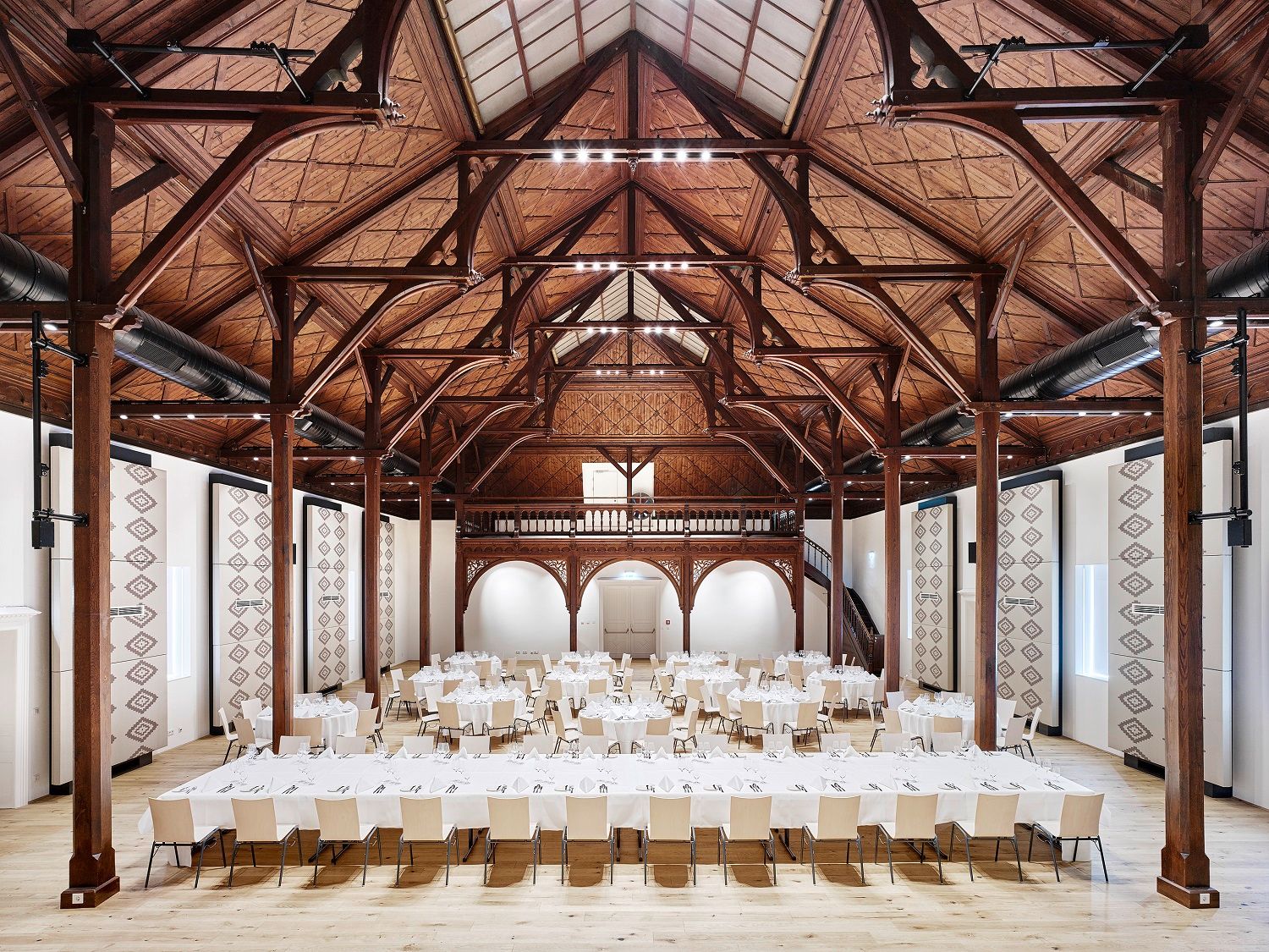 Interior view of a large banqueting hall with wooden beamed ceiling and covered tables.