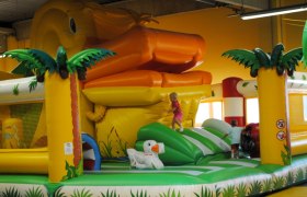 Aufblasbare Hüpfburg mit Riesenente und Palmen, Kinder spielen darauf.