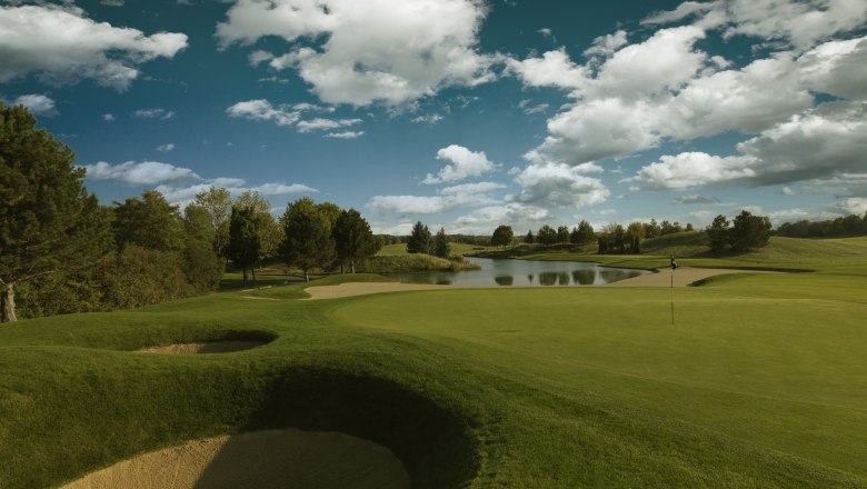 Golfplatz mit Sandbunker, Gr&uuml;n und Teich unter blauem Himmel mit Wolken.