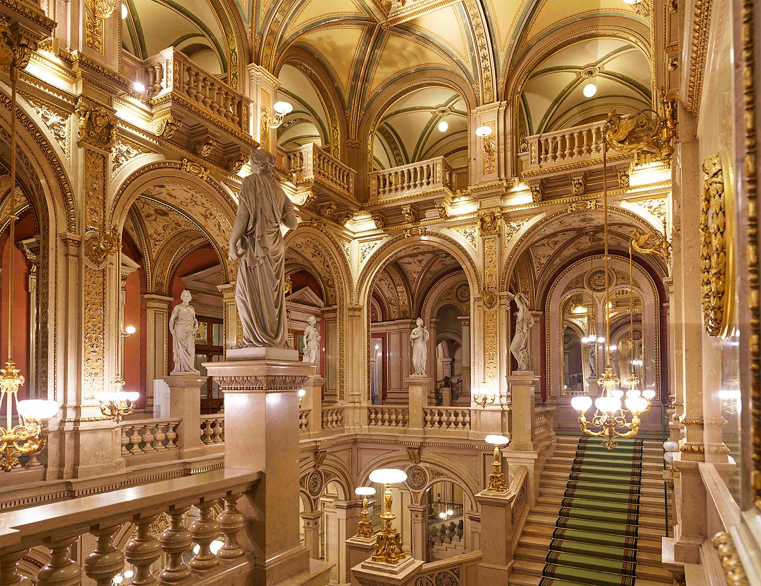 Prunkvolle Innenansicht der Wiener Staatsoper mit Statuen und verzierten Bögen.